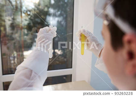 Caucasian schoolboy in lab coat and safety goggles watches fascination going on chemical reaction in test tubes. Learning chemistry and science. Back to school. Copy advertising space for text Caucasian schoolboy in lab coat and safety goggles watches fascination going on chemical reaction in test tubes. Learning chemistry and science. Back to school. Copy advertising space for text 93263228