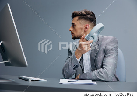 businessmen in headphones in a gray suit sits in front of a computer Gray background 93263985