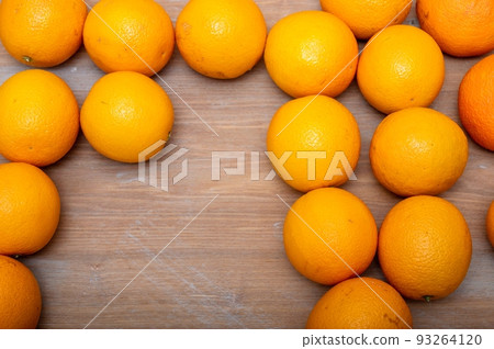 Orange ripe oranges lie on a textured wooden table in large quantities. Orange ripe oranges lie on a textured wooden table in large quantities. 93264120