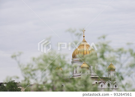 The outline of the large golden-domed dome of the Orthodox Christian Church of Christ the Savior through the trees and green foliage on a summer day. The outline of the large golden-domed dome of the Orthodox Christian Church of Christ the Savior through the trees and green foliage on a summer day. 93264561