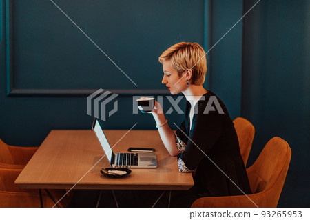 Businesswoman sitting in coffee shop at wooden table, drinking coffee and using laptop. Businesswoman browsing internet, chatting, blogging. Selective focus  93265953