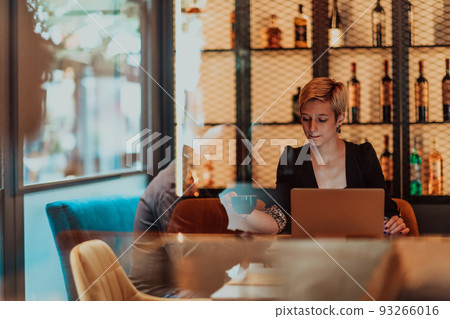 Businesswoman sitting in a cafe while focused on working on a laptop and participating in an online meetings. Selective focus. High quality photo 93266016