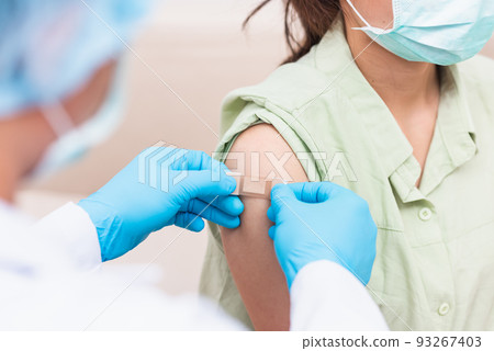 Doctor man after injection coronavirus vaccine to young woman shoulder he rubber protective gloves putting an adhesive bandage plaster Doctor man after injection coronavirus vaccine to young woman shoulder he rubber protective gloves putting an adhesive bandage plaster 93267403