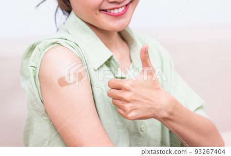 young woman showing gesturing thumb up or like and her arm with plaster band aid after coronavirus young woman showing gesturing thumb up or like and her arm with plaster band aid after coronavirus 93267404