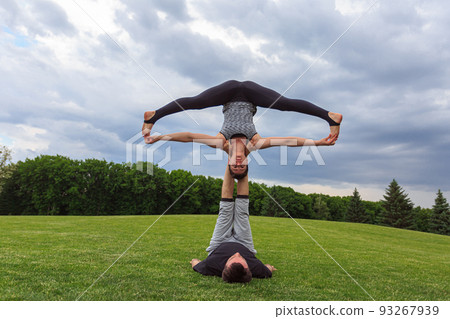 Young couple doing acro yoga in park. Man lying on grass and balancing woman in his feet 93267939
