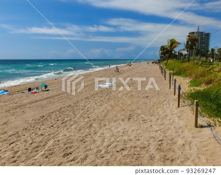 Long distance view of the sunny and tropical blue water shoreline with people, foliage, boats and buildings in the background seen from above the water. Long distance view of the sunny and tropical blue water shoreline with people, foliage, boats and buildings in the background seen from above the water. 93269247