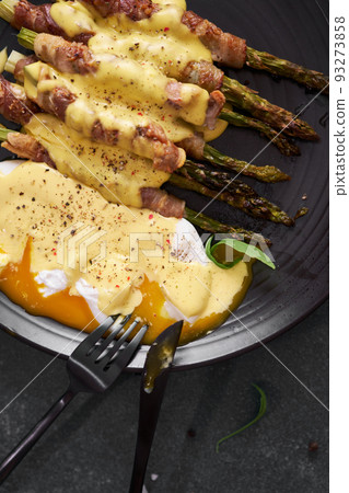 baked aspargus covered with bacon and poached eggs on a black ceramic plate baked aspargus covered with bacon and poached eggs on a black ceramic plate 93273858