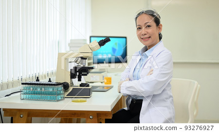 Shot of middle aged scientist sitting in front of microscope at research laboratory and smiling to camera Shot of middle aged scientist sitting in front of microscope at research laboratory and smiling to camera 93276927