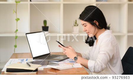 Side view asian woman employee sitting at her office desk and typing text message, chatting online on mobile phone Side view asian woman employee sitting at her office desk and typing text message, chatting online on mobile phone 93276983