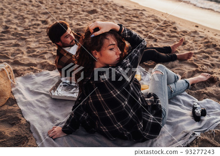 Young couple having picnic on the beach at dawn, woman and man meeting sunrise together on the sea 93277243