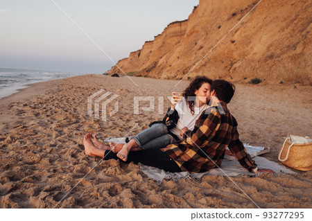 Young couple kissing on the beach at dawn, woman and man meeting sunrise together on the sea with scenic coastline on the background 93277295