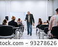 During a physics test in college, a professor in a jacket walks around the audience and communicates with students who write and answer questions 93278626