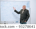 An elderly professor of mathematics stands in his office at a white board with notes and explains the material to students 93278641