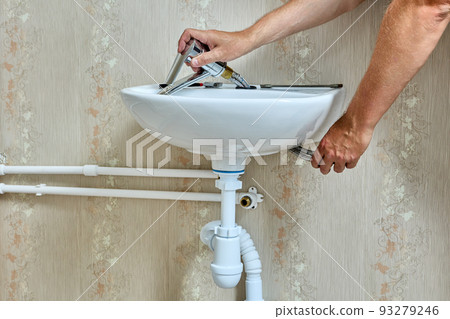 Plumbing work with home water supply system, plumber installs faucet on sink in bathroom. 93279246