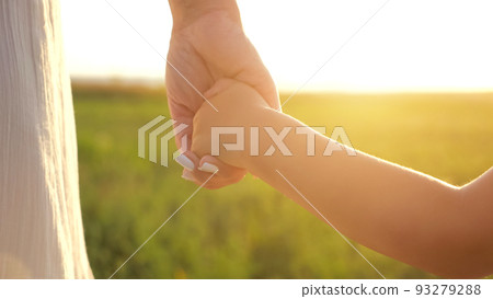 Child takes mother hand against blurry green meadow 93279288