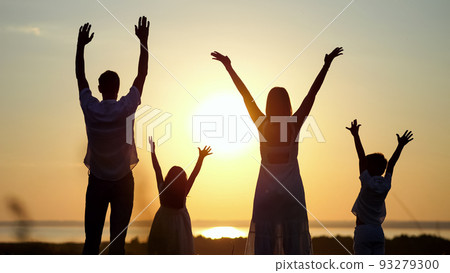 Family looks at sunset raising hands to sky on meadow Family looks at sunset raising hands to sky on meadow 93279300