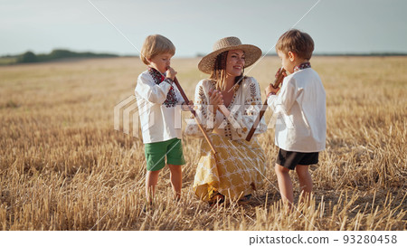 Boys playing on wooden flutes - sopilka. Ukrainian mother with children sons in wheat field. Woman Boys playing on wooden flutes - sopilka. Ukrainian mother with children sons in wheat field. Woman 93280458