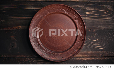Empty ukrainian clay plate from wooden table. Top view. National tableware with handmade ornament Empty ukrainian clay plate from wooden table. Top view. National tableware with handmade ornament 93280473