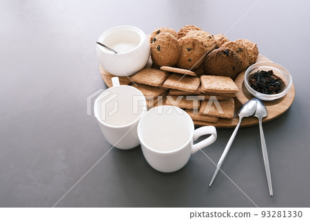 A tasty snack two cups of black tea and a plate of oatmeal cookies a wooden board on the gray background, leaf tea. A tasty snack two cups of black tea and a plate of oatmeal cookies a wooden board on the gray background, leaf tea. 93281330