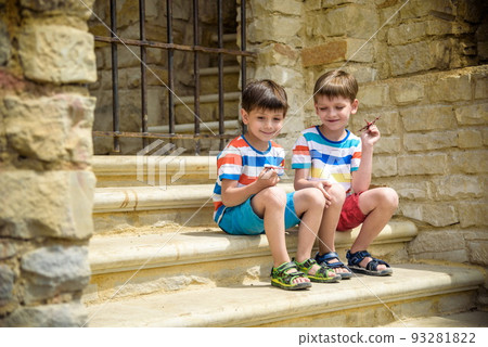 The children playing on the ruins of ancient building with metal gate an archaeological site of an ancient city. Two boys sitting and play with toy aircraft plane. Travel concept The children playing on the ruins of ancient building with metal gate an archaeological site of an ancient city. Two boys sitting and play with toy aircraft plane. Travel concept 93281822