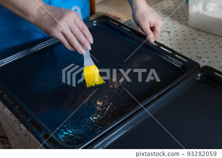 Woman oiling baking sheet. Baking at home. Woman oiling baking sheet. Baking at home. 93282059