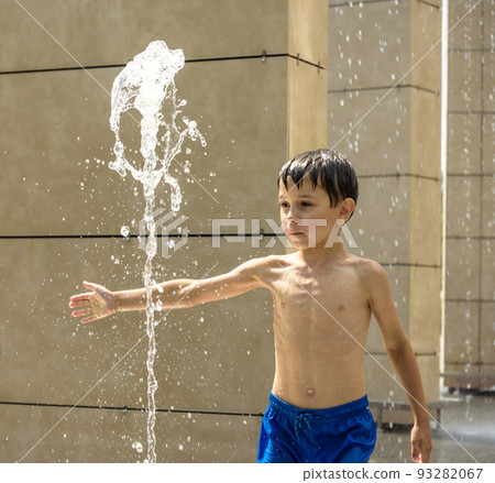Boy having fun in water fountains. Child playing with a city fountain on hot summer day. Happy kids having fun in fountain. Summer weather. Active leisure, lifestyle and vacation 93282067