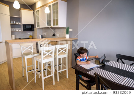 Smart preteen schoolboy doing his homework with digital tablet at home. Child using gadgets on his kitchen to study. Modern education and learning for kids Smart preteen schoolboy doing his homework with digital tablet at home. Child using gadgets on his kitchen to study. Modern education and learning for kids 93282069