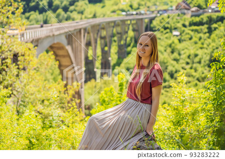 Montenegro. Woman tourist in background of Dzhurdzhevich Bridge Over The River Tara. Travel around Montenegro concept. Sights of Montenegro Portrait of a disgruntled girl sitting at a cafe table 93283222