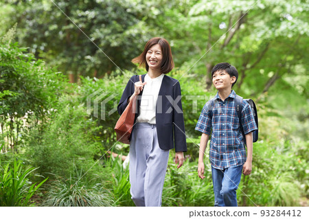 一個男孩的小學生和他的母親邊走邊笑著說話 一個男孩的小學生和他的母親邊走邊笑著說話 93284412