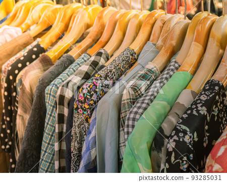 Bright colored clothes on wooden hangers on the market, Clothes shop in the outdoor market, Clothing trade. Bright colored clothes on wooden hangers on the market, Clothes shop in the outdoor market, Clothing trade. 93285031