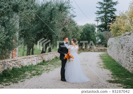 Happy stylish smiling couple walking in Tuscany, Italy on their wedding day. The bride and groom walk down the street by the hands. A stylish young couple walks. Husband and wife communicate nicely Happy stylish smiling couple walking in Tuscany, Italy on their wedding day. The bride and groom walk down the street by the hands. A stylish young couple walks. Husband and wife communicate nicely 93287042