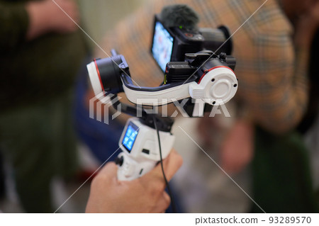 Professional videographer in black hoodie holding professional camera on 3-axis gimbal stabilizer. Filmmaker making a great video with a professional cinema camera. Cinematographer. Professional videographer in black hoodie holding professional camera on 3-axis gimbal stabilizer. Filmmaker making a great video with a professional cinema camera. Cinematographer. 93289570