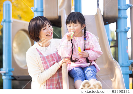 A girl and a nursery teacher playing with soap bubbles in the park 93290321