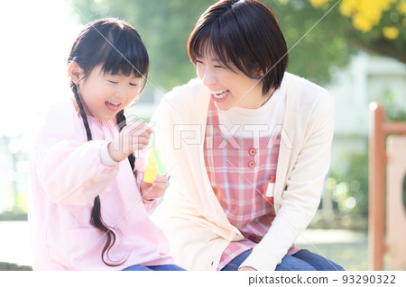 A girl and a nursery teacher playing with soap bubbles in the park 93290322