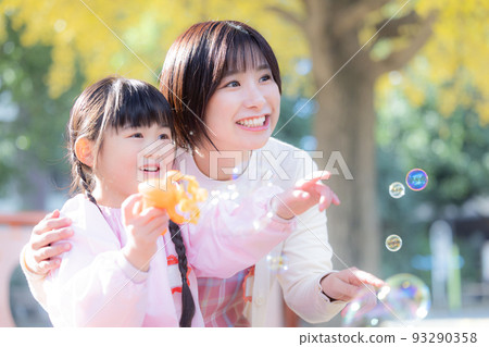 A girl and a nursery teacher playing with soap bubbles in the park A girl and a nursery teacher playing with soap bubbles in the park 93290358