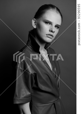 Seasonal Sale offer. Confidence blond young lady in trendy leather trench coat dress looks with blue eyes at camera presenting evening makeup posing isolated on olive green studio wall background 93290595