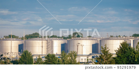 Fuel storage tanks view, oil refinery plant in morning daylight against green summer trees and blue sky Fuel storage tanks view, oil refinery plant in morning daylight against green summer trees and blue sky 93291979