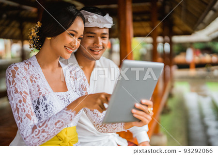 balinese man and woman in kebaya using tablet pc 93292066