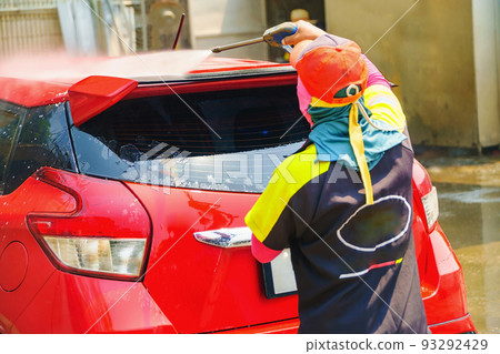 Car wash service., Self-cleaning car wash., The young man was washing the car to be clean and safe from germs., The young man is spraying the water on the roof of the car for cleanliness. 93292429