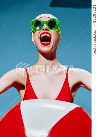 Vacation concept. A screaming unusual lady in a swimming cap with a red white ball on a blue background Vacation concept. A screaming unusual lady in a swimming cap with a red white ball on a blue background 93296221