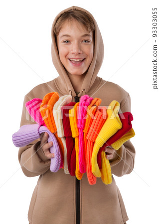 Laughing teenager, in a brown hoodie, with a hood on his head, with a stack of colored knitted hats in his hands, isolate Laughing teenager, in a brown hoodie, with a hood on his head, with a stack of colored knitted hats in his hands, isolate 93303055