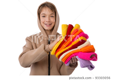 Happy teenager, in a brown sports jacket, with a hood on his head, with a bunch of colored knitted hats in his hands, isolate Happy teenager, in a brown sports jacket, with a hood on his head, with a bunch of colored knitted hats in his hands, isolate 93303056