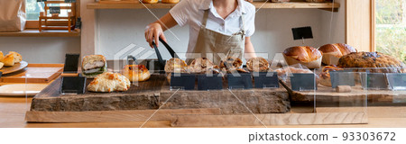Bakery bakery shop A female clerk in an apron holding freshly baked bread with tongs 93303672