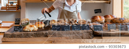 Bakery bakery shop A female clerk in an apron holding freshly baked bread with tongs 93303673