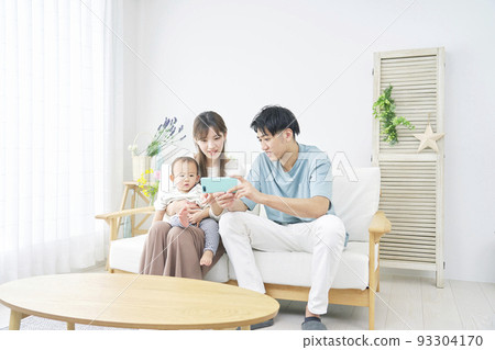 Parents and baby looking at smartphone in living room 93304170