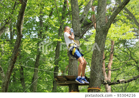 Male junior high school student (12 years old) playing on an athletic zip line on a tree 93304216