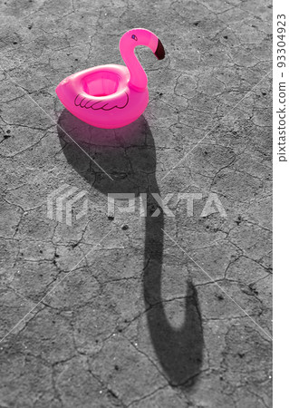 pink inflatable flamingo stands on dry monochrome ground with cracks, toy casts a long shadow 93304923