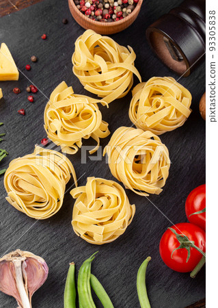 Raw pasta tagliatelle with fresh tomatoes, peppers, mushrooms,asparagus beans, spices and cheese on black table. 93305838