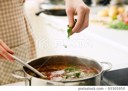 A woman in an apron adds spices to borscht. A woman in an apron adds spices to borscht. 93305950