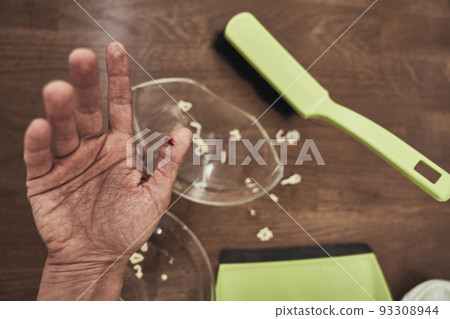 Selective focus on a cut female finger on the background of a split cup and a brush with a dustpan for cleaning. A wound with blood received when cleaning broken dishes. High quality photo 93308944